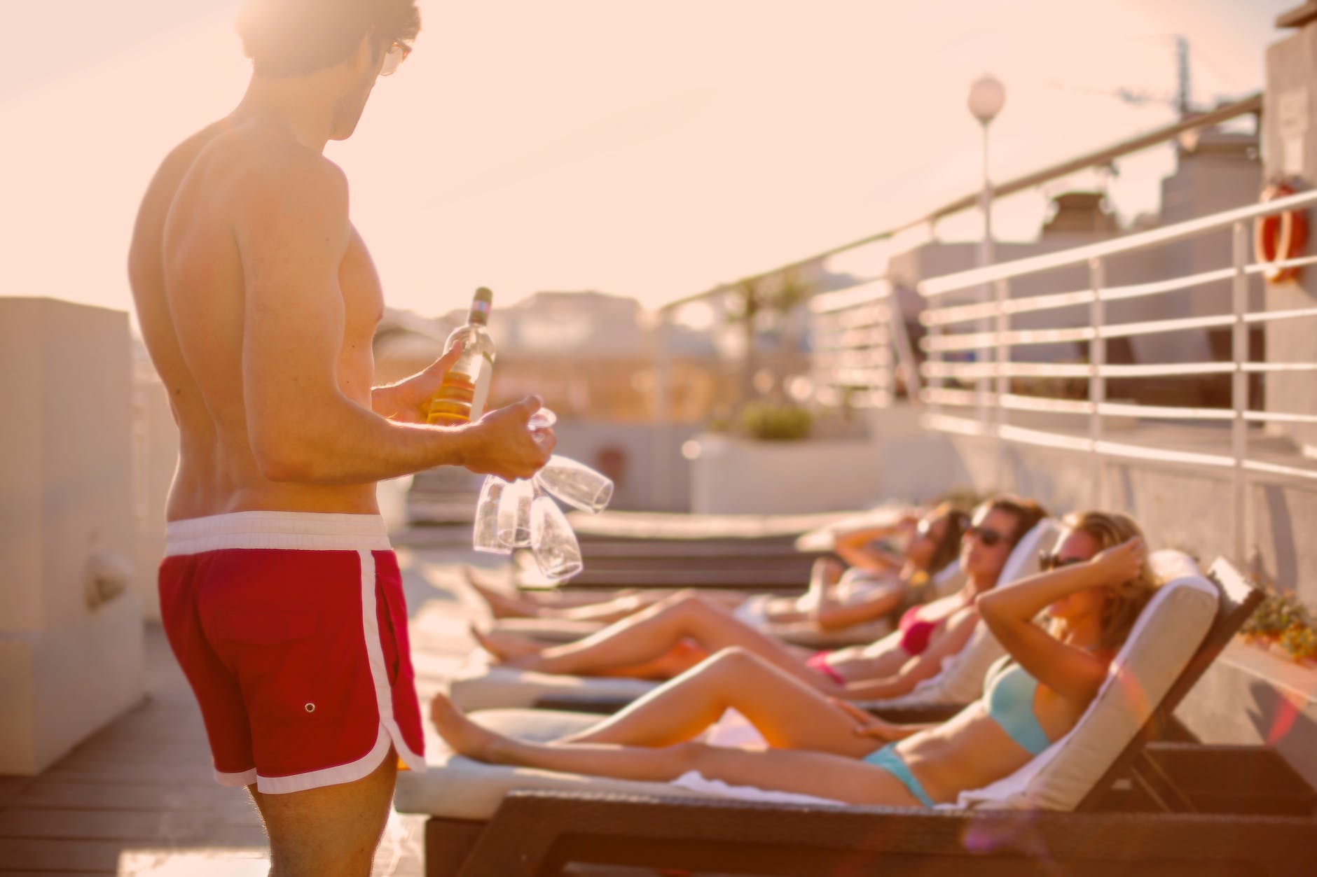 young man offering drinks to sunbathing girlfriends